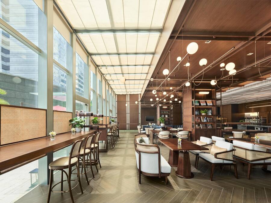 A modern interior with a long dining table, multiple seating arrangements, and a large window providing a view of the city.