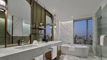 A modern bathroom with a large mirror, two sinks, a bathtub, and a city view.