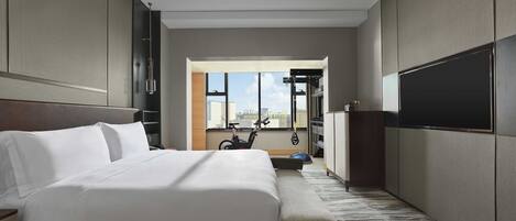 A modern hotel room with a large bed, a TV, and a view of the city through a large window.