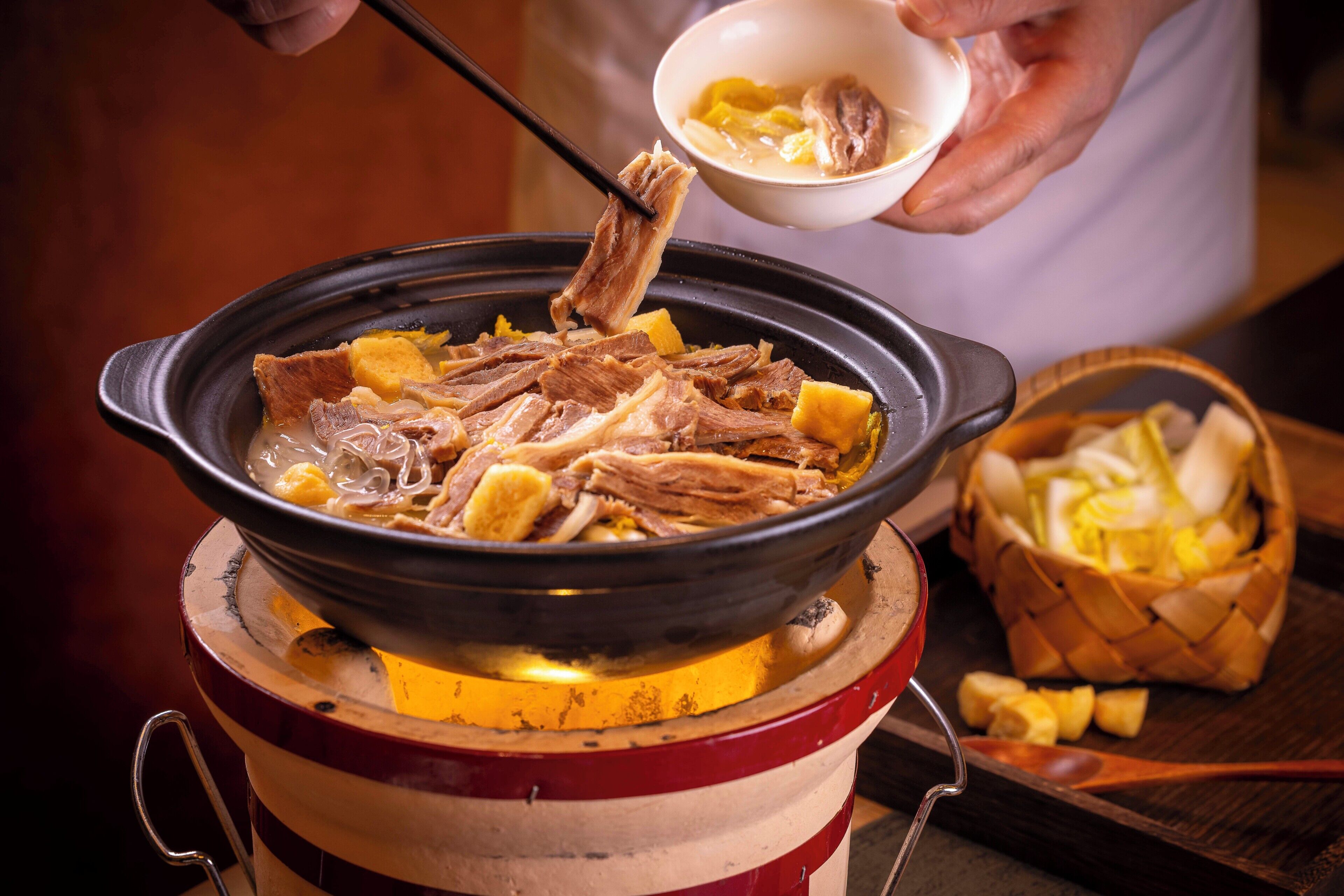 A person cooking meat and vegetables in a traditional pot over an open flame.