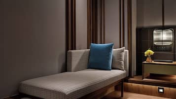 A modern hotel room with a sofa bed, a bedside table with a vase of flowers, and a wall-mounted light fixture.