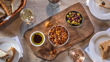 Una mesa de madera con diversos alimentos, como pan, aceitunas y frutos secos, junto con copas de vino.