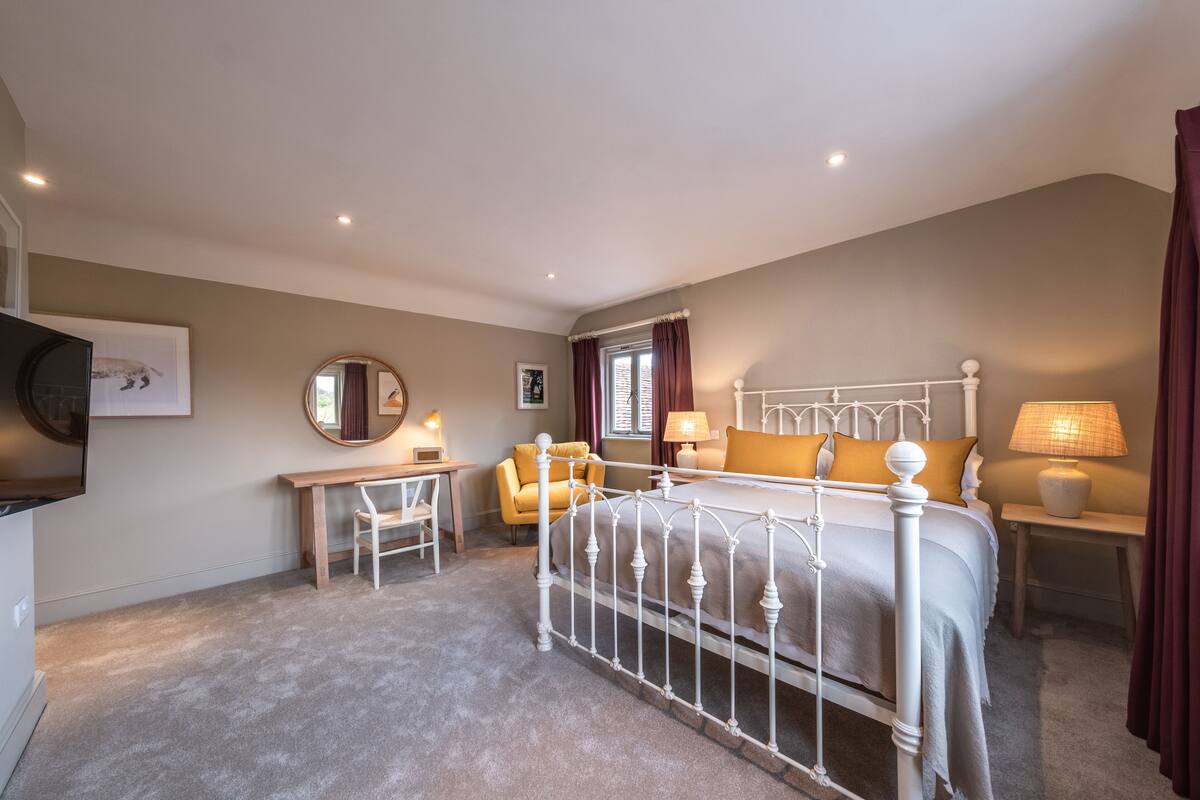 Een slaapkamer met een bed met een wit metalen frame, een nachtkastje met een lamp, een stoel en een bureau met een lamp.