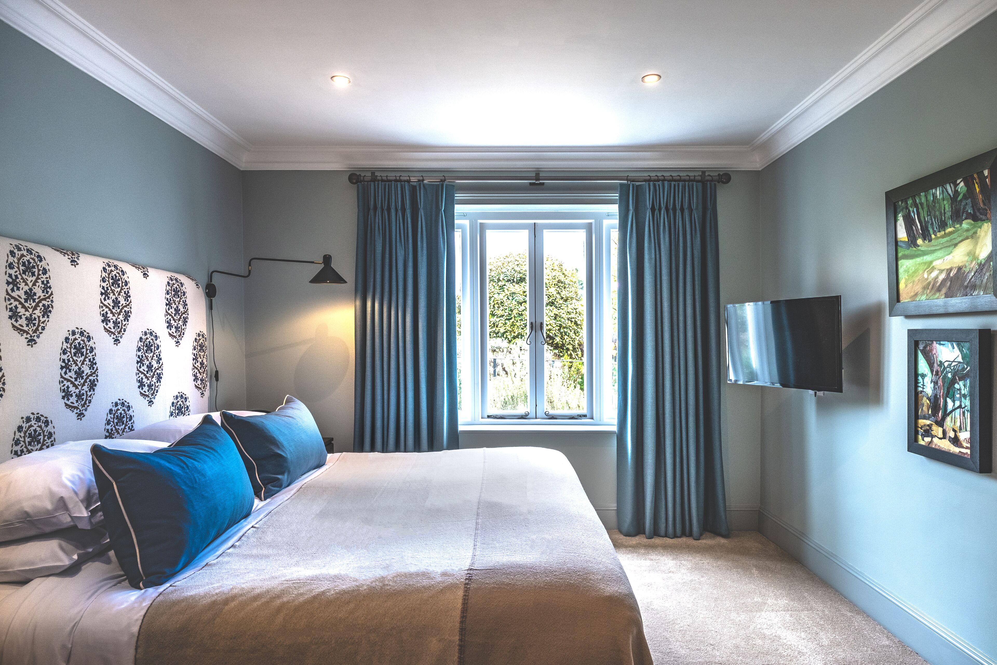 A bedroom with a large bed, a flat-screen TV mounted on the wall, and a window with curtains.