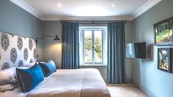 A bedroom with a large bed, a flat-screen TV mounted on the wall, and a window with curtains.
