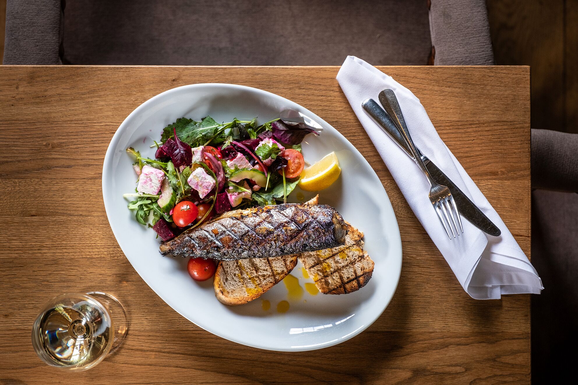 Un plato de pescado a la parrilla con una ensalada y una rodaja de limón sobre una mesa de madera.