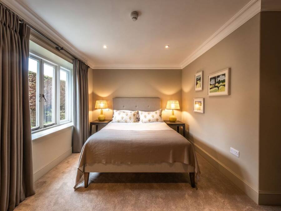 Un dormitorio con una cama grande, dos lámparas de noche, una ventana con cortinas y cuadros en la pared.