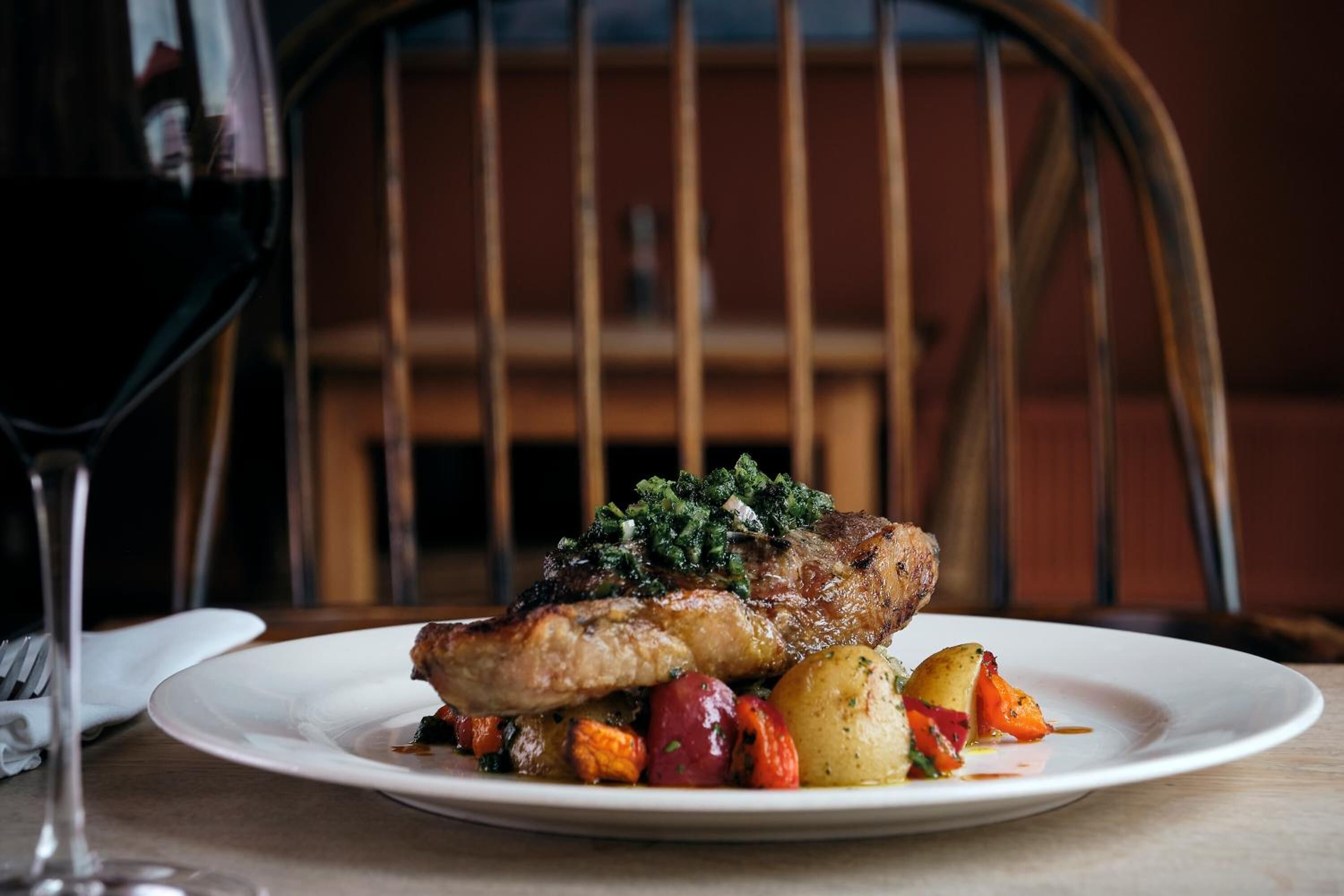 Ein Teller mit Essen, darunter ein Steak, Kartoffeln und Gemüse, dazu ein Glas Rotwein.