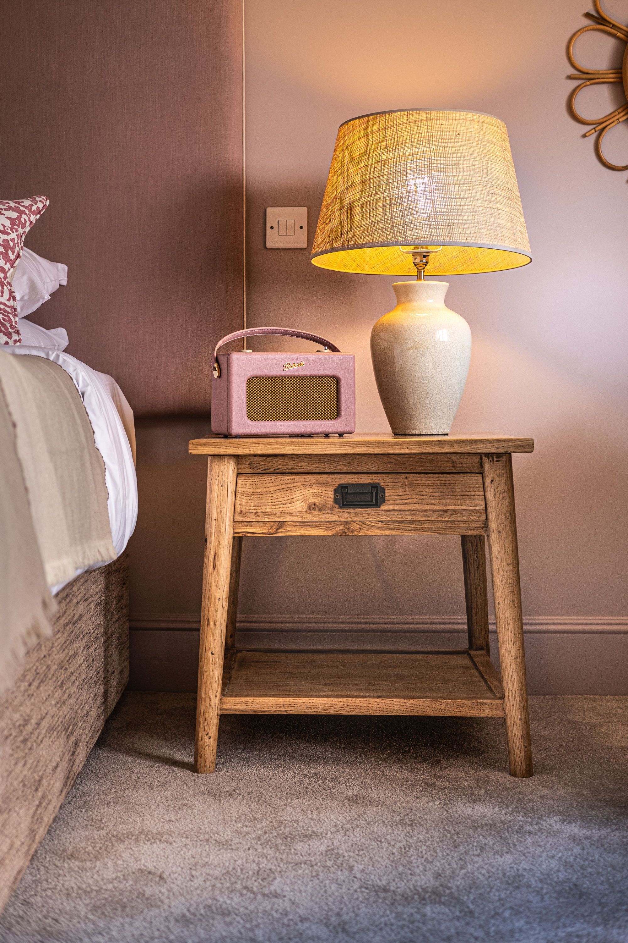 A wooden bedside table with a lamp and a vintage radio.