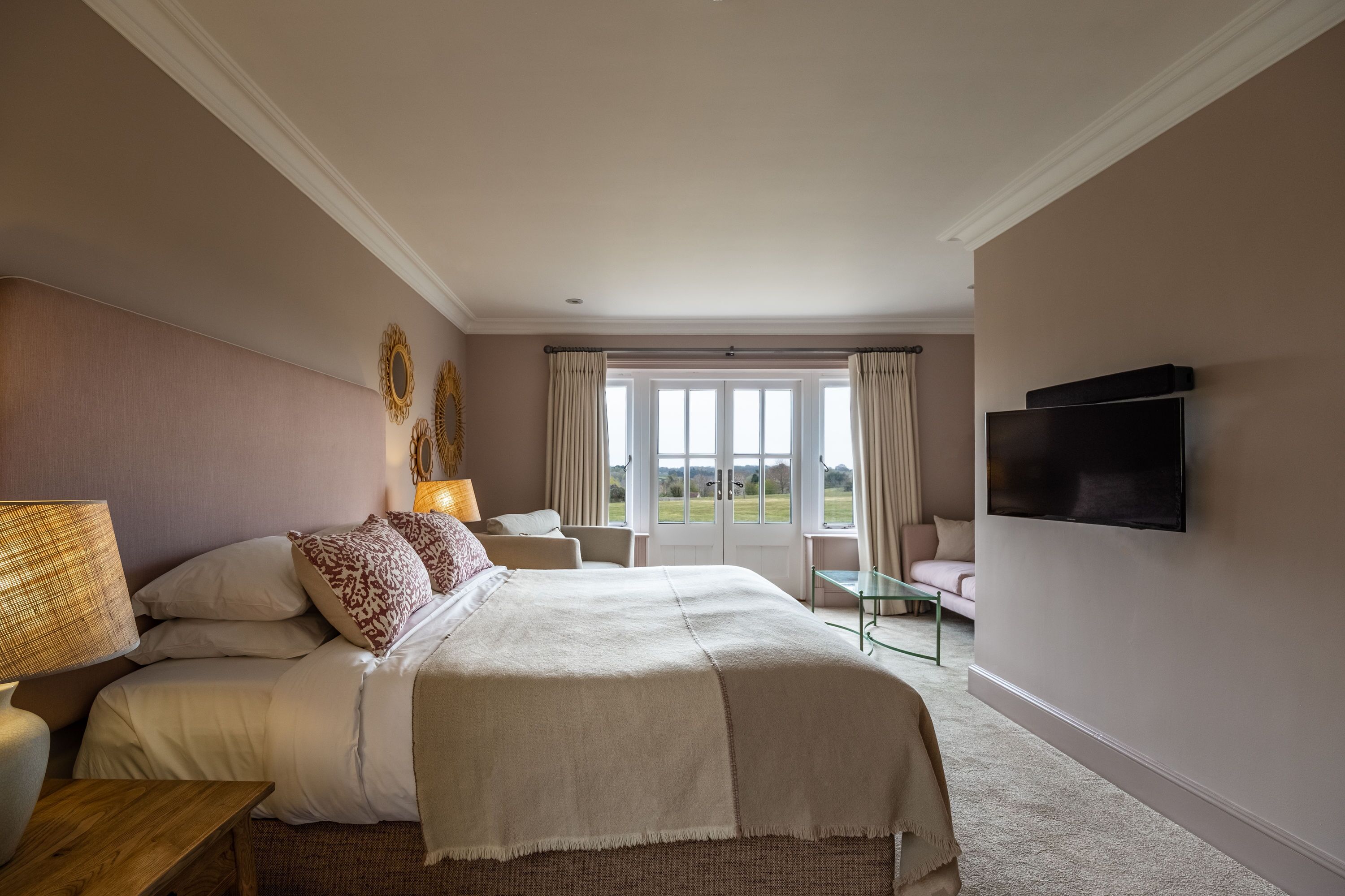 A bedroom with a large bed, a TV mounted on the wall, and a view of the outdoors through the window.