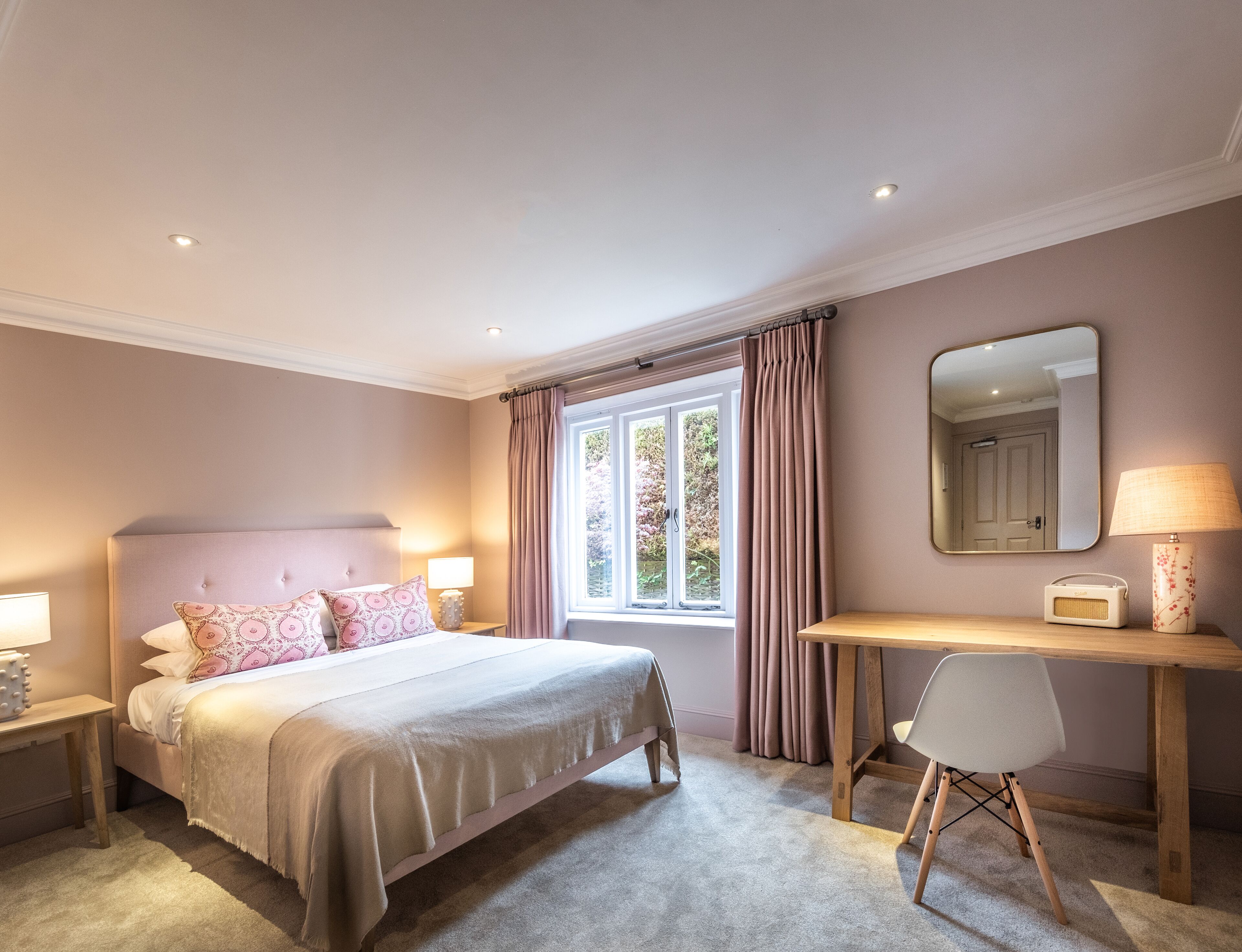 A bedroom with a bed, bedside tables, a desk, a chair, a window with curtains, and a mirror on the wall.