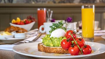 Un desayuno con tostadas cubiertas de aguacate, un huevo poché y tomates cherry. También hay tazones de fruta y un vaso de jugo de naranja.