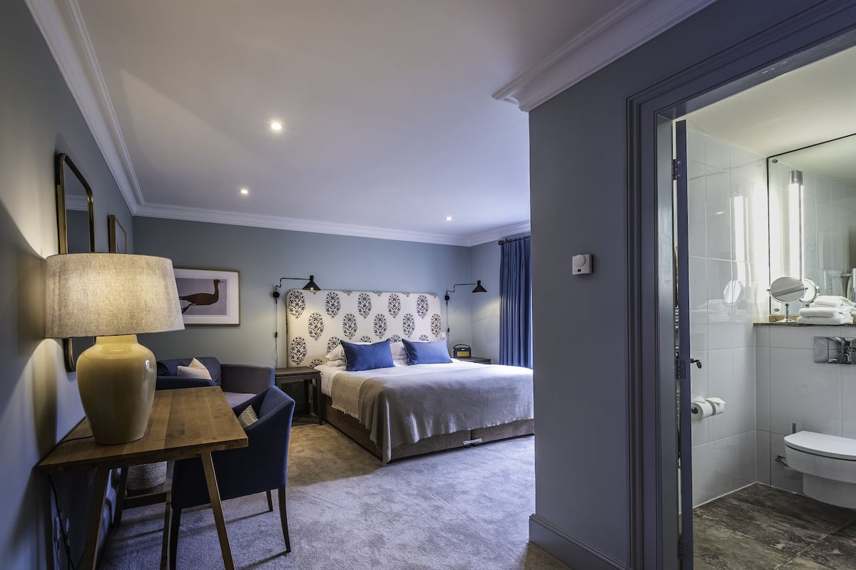 Een hotelkamer met een bed, nachtkastje, lamp en uitzicht op de badkamer.