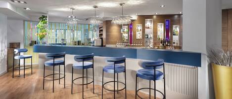 A modern bar area with wooden flooring, blue bar stools, and a variety of bottles and glasses on shelves.