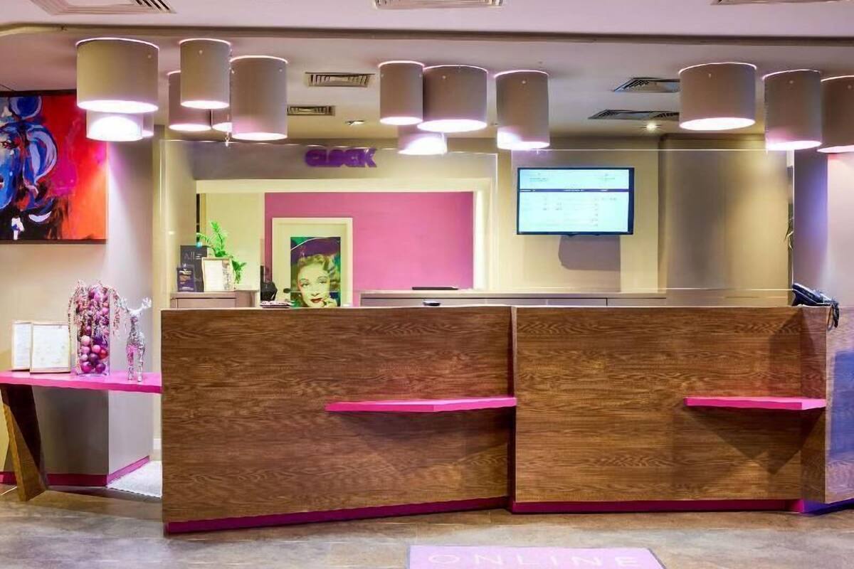A reception desk with a pink and wooden design, a digital screen, and a plant.