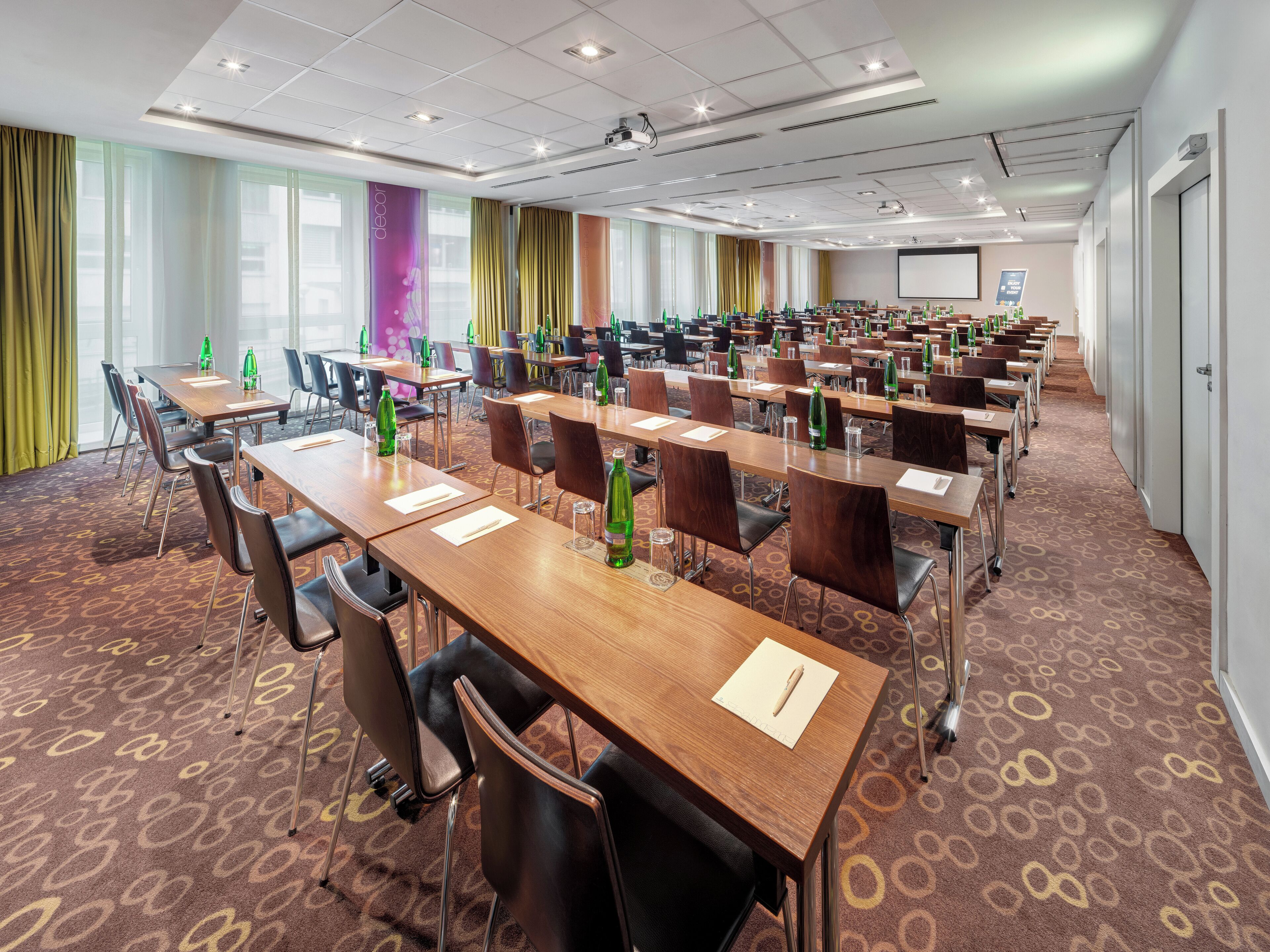 A conference room with multiple tables, chairs, and a projector screen.