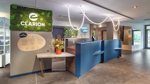 Zona de recepción con un letrero de 'Clarion', un mostrador de recepción, una planta y una pantalla digital.