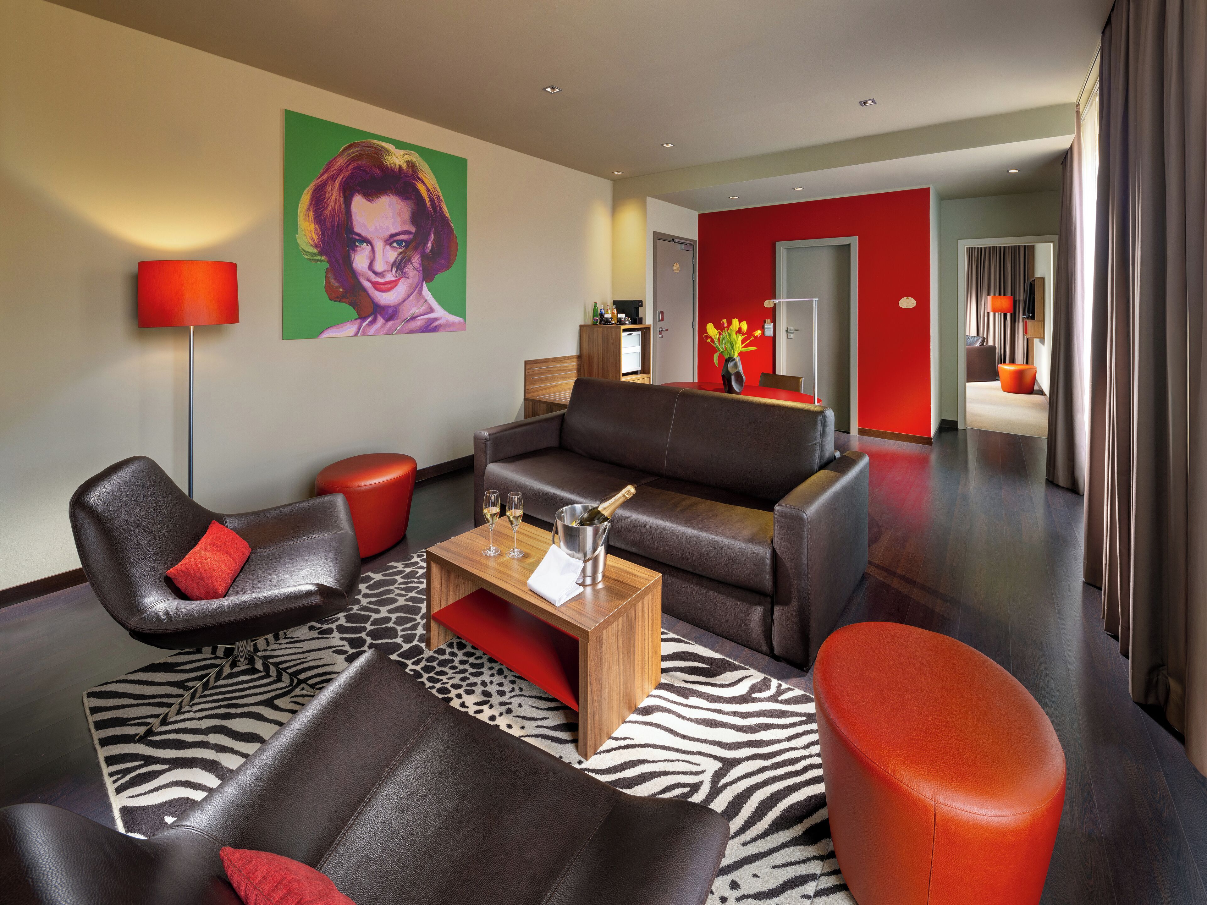 A modern living room with leather sofas, a zebra-patterned rug, and a red accent wall.