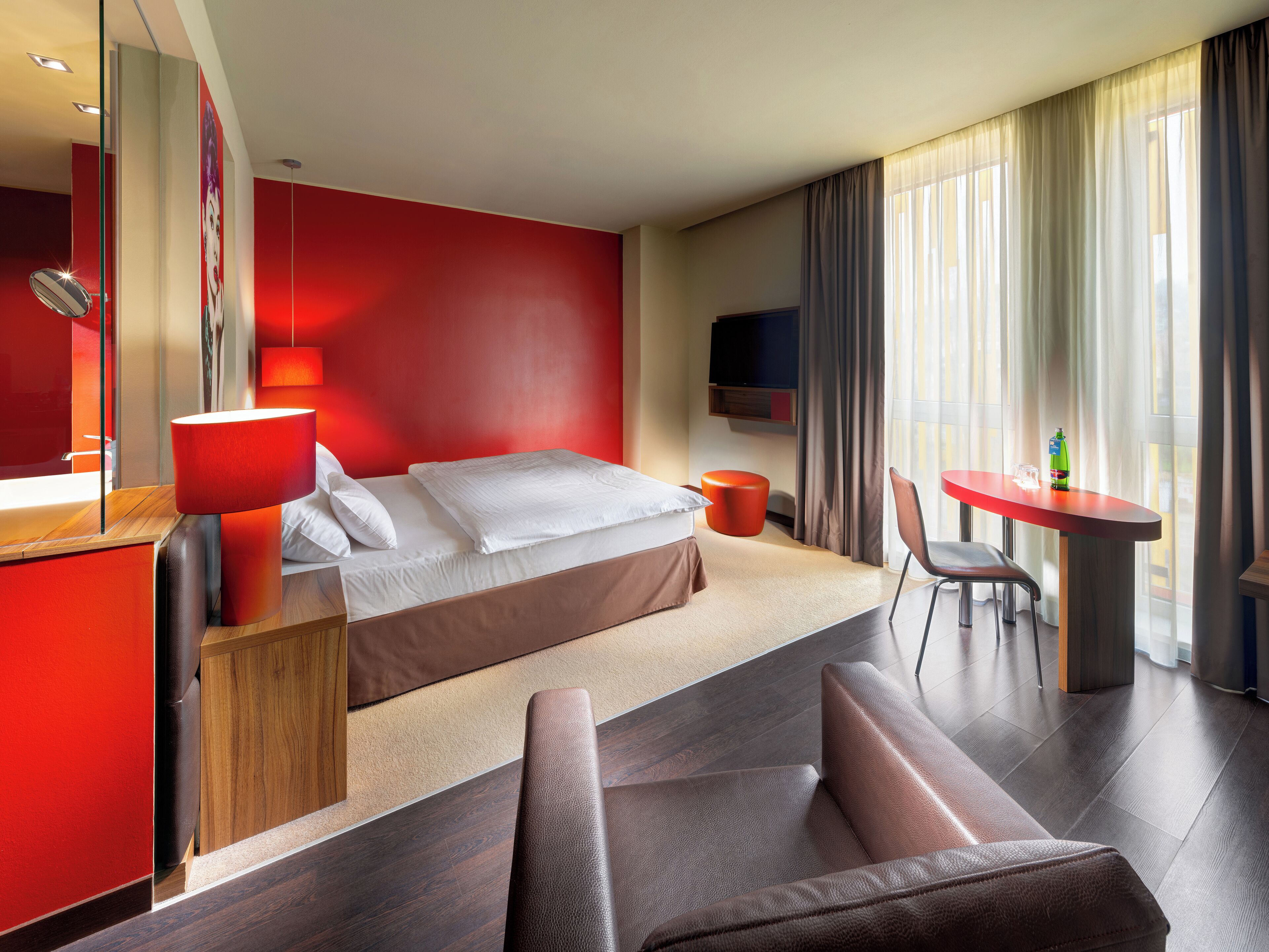 Moderni hotellihuone, jossa on sänky, työpöytä, tuoli ja televisio.