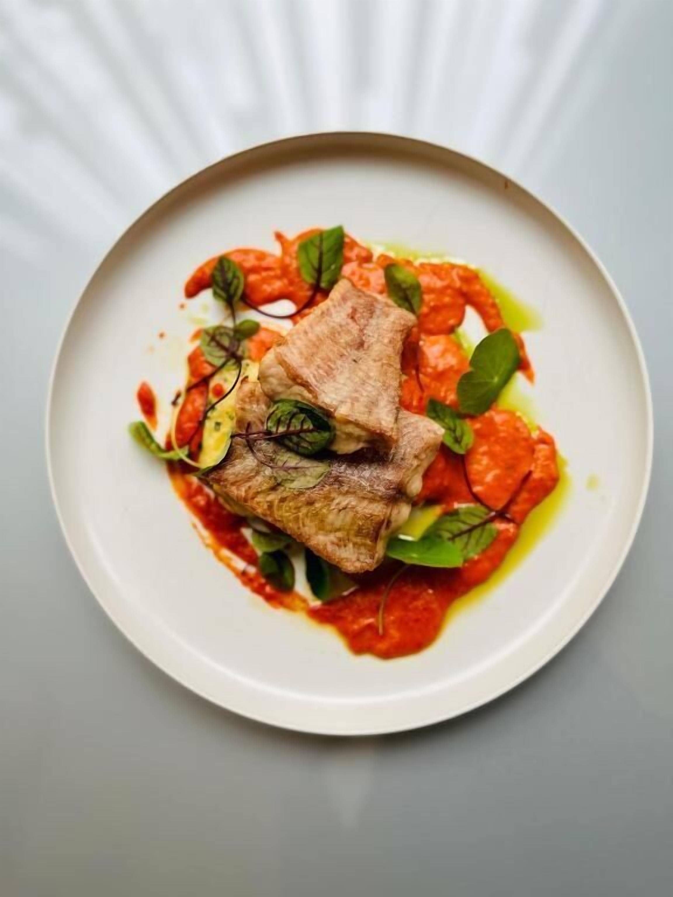 A plate with a piece of meat, greens, and a red sauce.