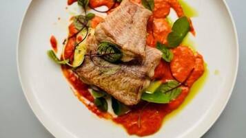 A plate with a piece of meat, greens, and a red sauce.