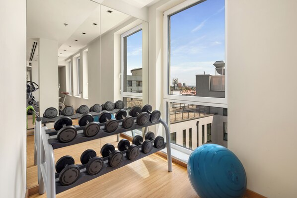 A gym with a rack of dumbbells, a blue exercise ball, and large windows offering a view of the city. - Clarion Congress Hotel Bratislava (Bratislava)