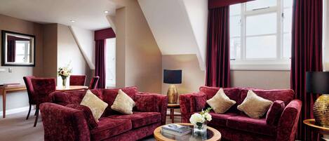 A modern living room with two red velvet sofas, a wooden coffee table, and a large window with curtains.
