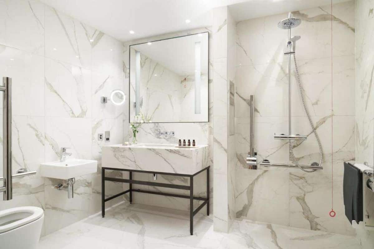 A modern bathroom with a marble sink, a large mirror, a handheld showerhead, and a toilet.