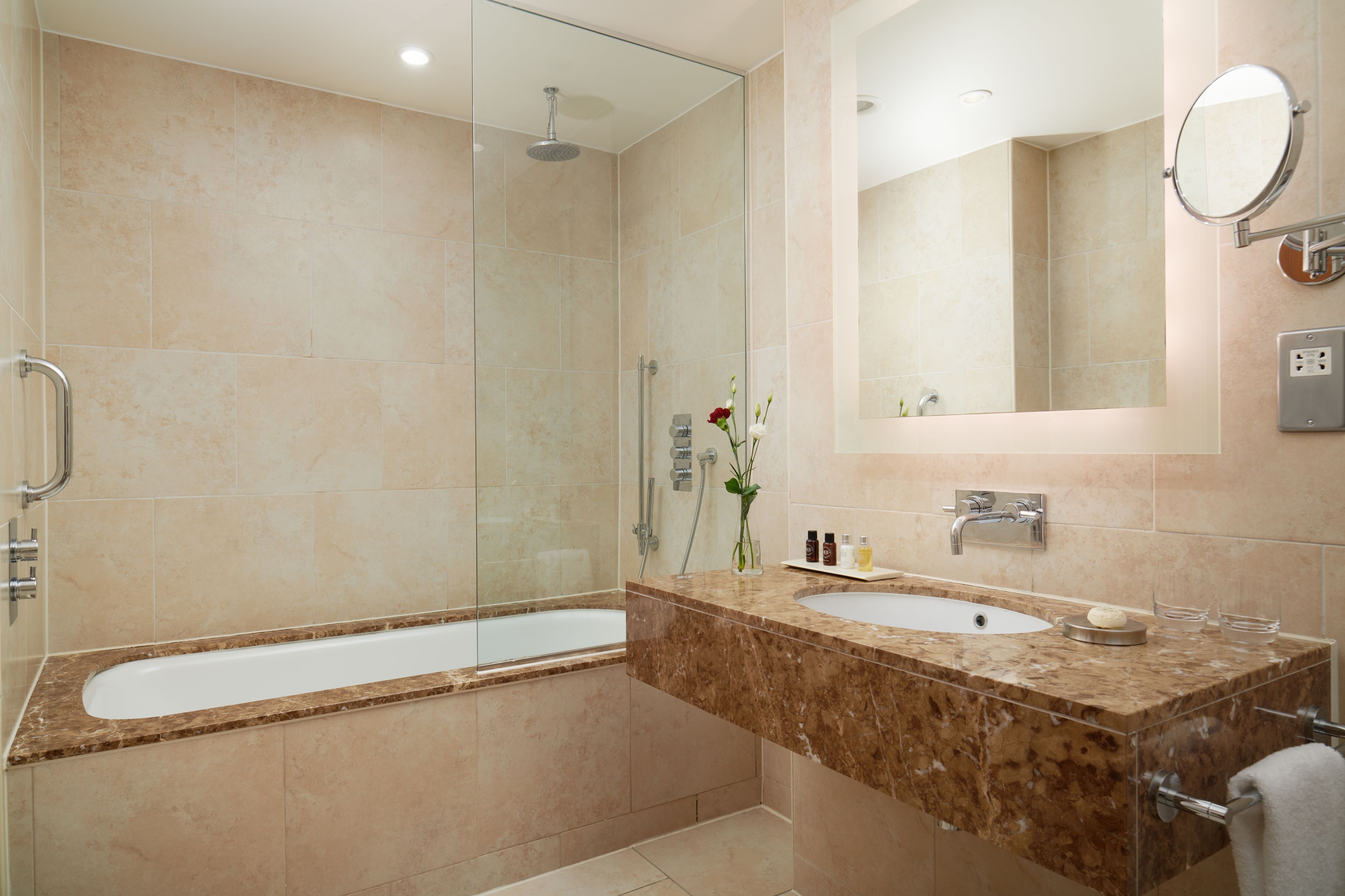 Un baño moderno con ducha envuelta en vidrio, una bañera independiente y un tocador de mármol con lavabo y espejo.