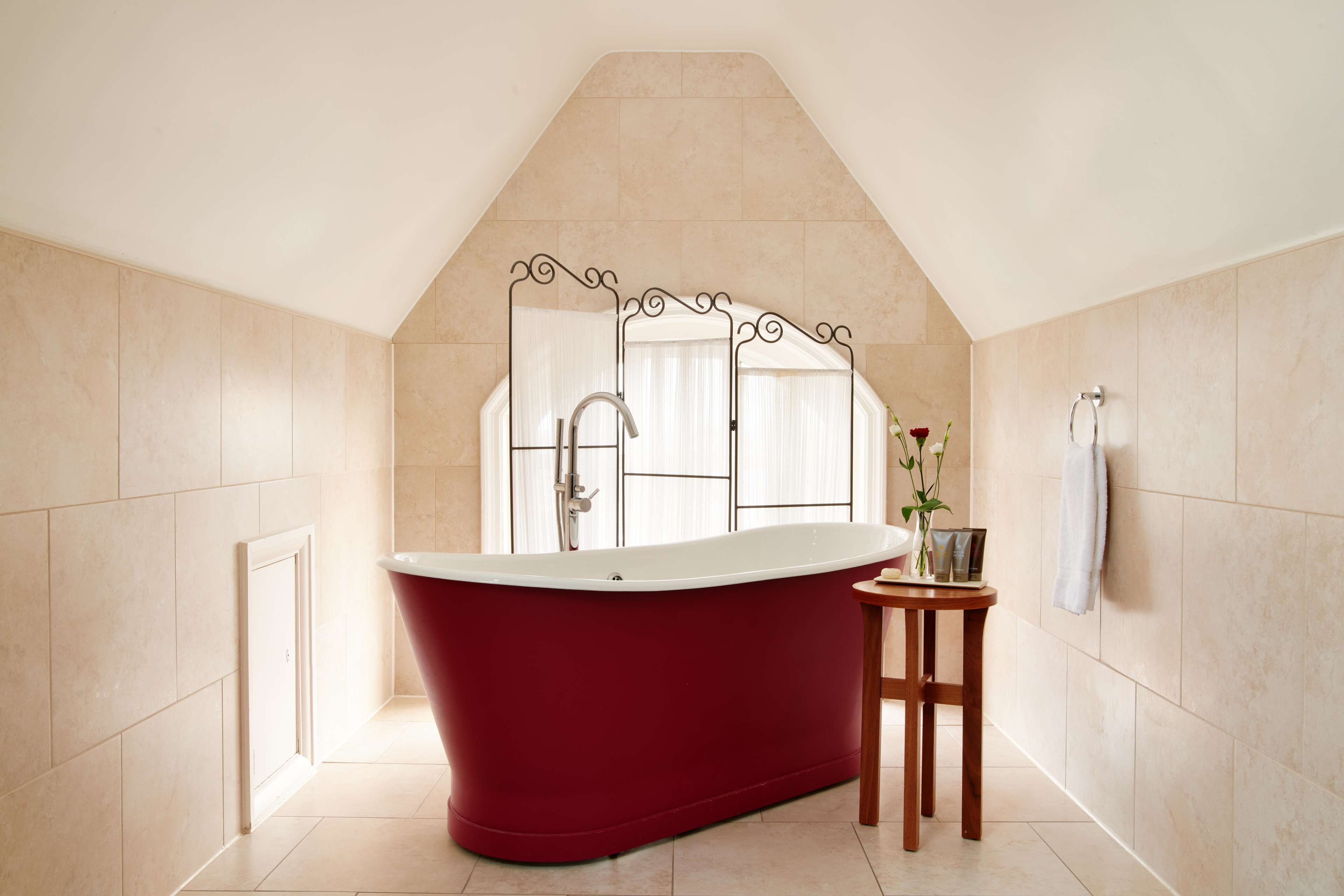Une salle de bain moderne avec une baignoire sur pieds, un meuble-lavabo avec un miroir et une petite table agrémentée d’un vase de fleurs.
