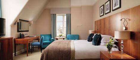 A hotel room with a bed, a desk, a chair, a TV, and a window with curtains.