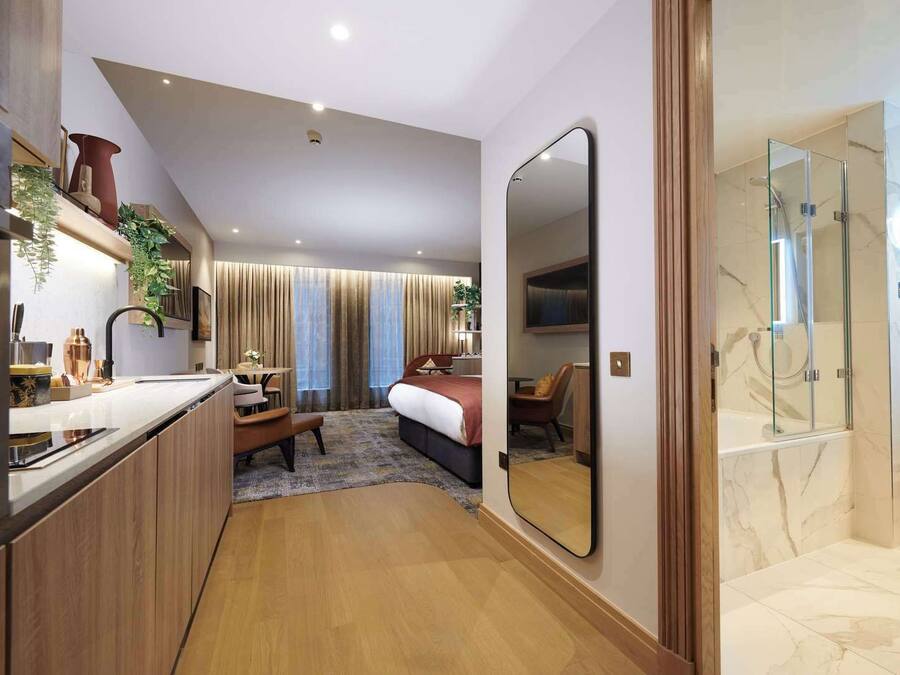 A modern hotel room with a kitchenette, a bed, a seating area, and a shower area.
