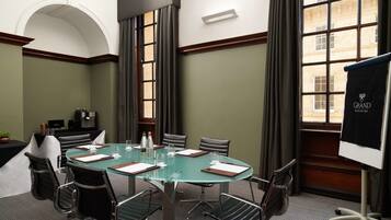 A conference room with a glass table, black leather chairs, a whiteboard, and a view of a building through large windows.