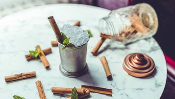 Ein Martini-Glas mit Eiswürfeln und einem Minzblatt auf einer Marmorplatte, umgeben von Zimtstangen und einer Flasche.