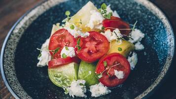Une assiette de nourriture comprenant des tomates en tranches, du fromage et des légumes verts, le tout présenté sur une assiette foncée.