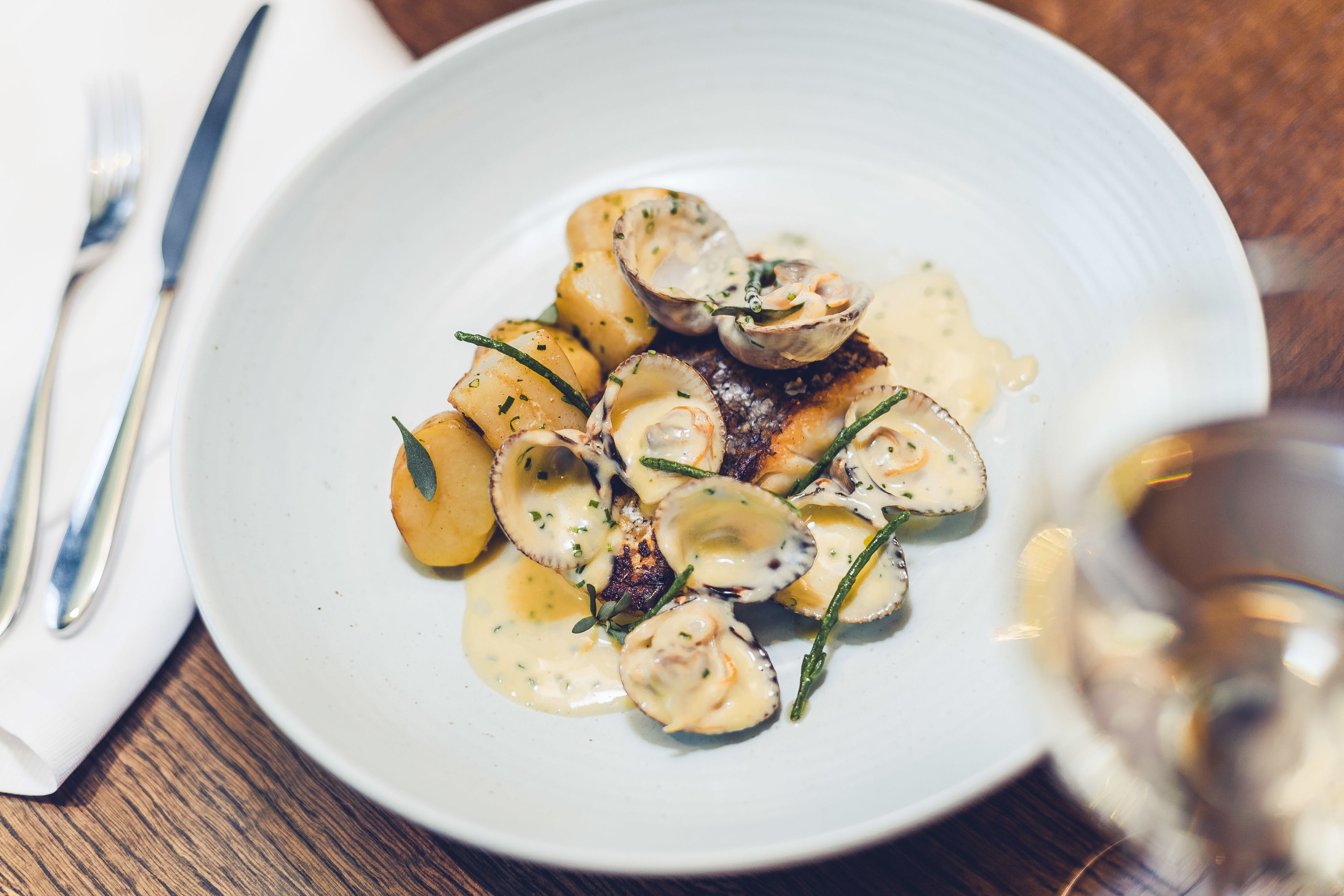 A white plate with a seafood dish, possibly scallops, accompanied by potatoes and garnished with herbs.