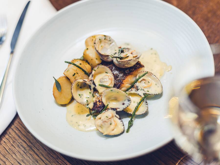 A white plate with a seafood dish, possibly scallops, accompanied by potatoes and garnished with herbs.