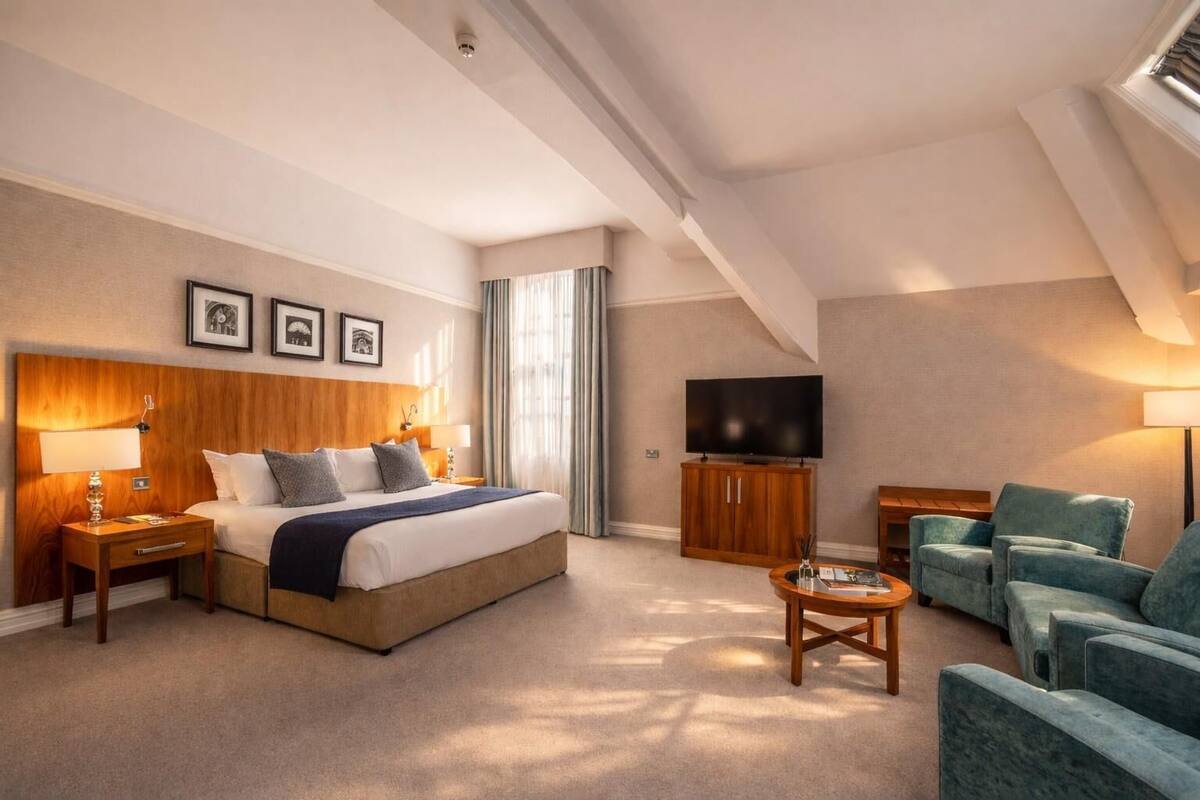 Hotellihuone, jossa on suuri sänky, televisio, työpöytä ja oleskelualue tuoleineen.
