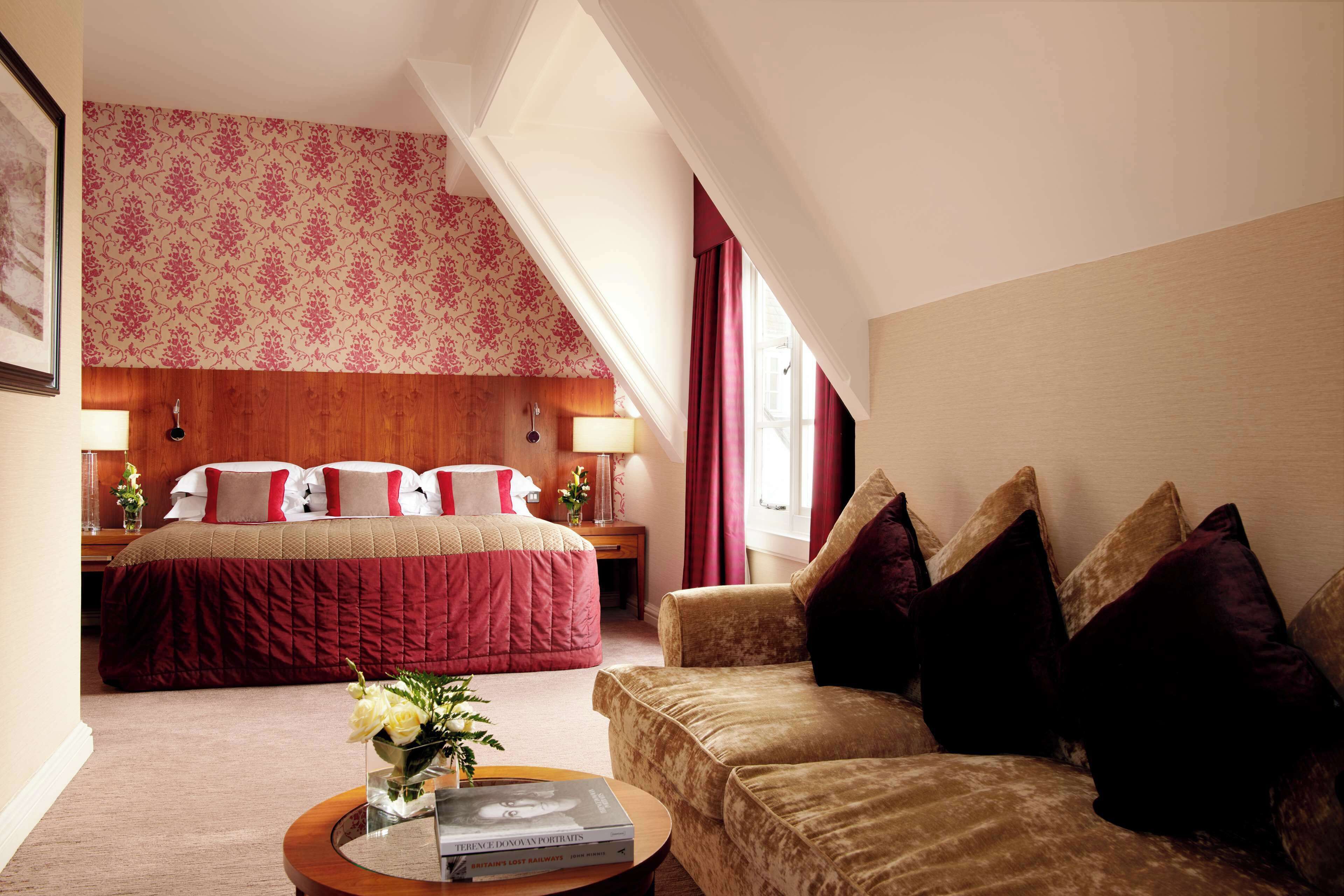 A hotel room with a large bed, a sofa, a small table with a book, and a window with curtains.
