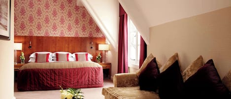 A hotel room with a large bed, a sofa, a small table with a book, and a window with curtains.