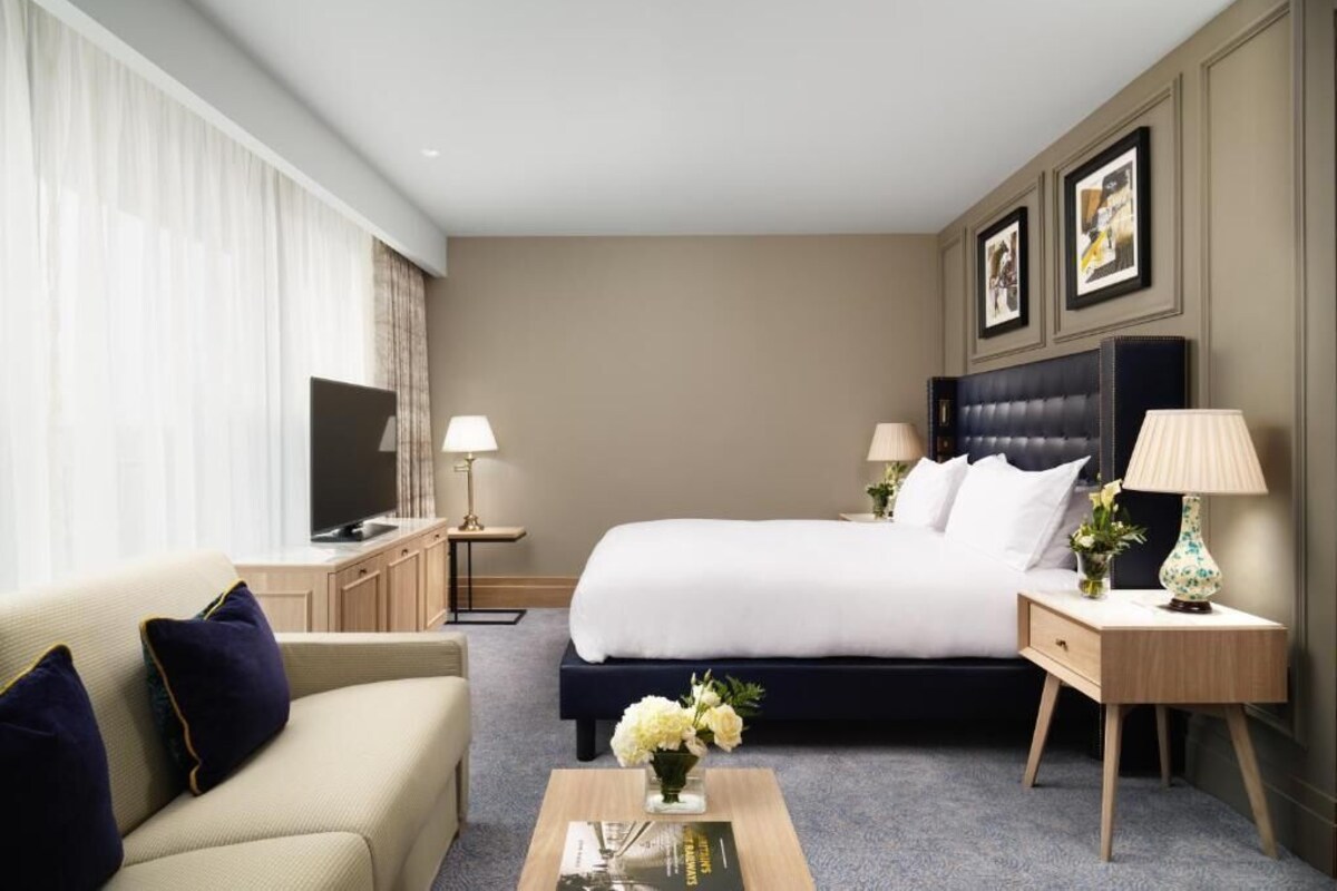 A hotel room with a large bed, a sofa, a TV, and a desk with lamps.