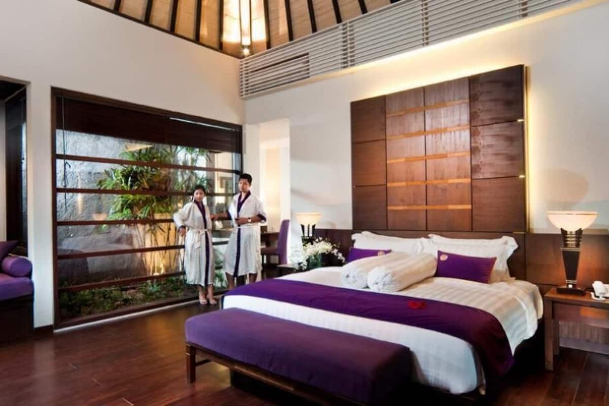 Une chambre d’hôtel moderne dotée d’un grand lit, d’un canapé, d’une grande fenêtre offrant une vue agréable et d’une tête de lit en bois.