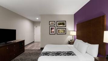 Habitación de hotel con cama, televisor, cómoda, mesita de noche, lámpara y cuadros en la pared.