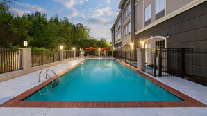 Piscina retangular com escada de metal, rodeada por um deck de tijolos e uma cerca de metal.