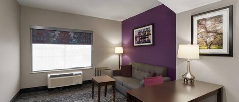A hotel room with a large window, a sofa, a table, a lamp, and a framed picture on the wall.