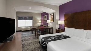 Quarto de hotel com cama, escrivaninha, cadeira, televisão e janela com persianas.