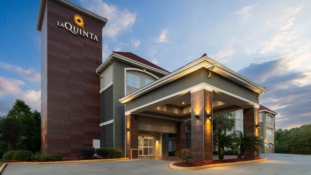 Um hotel com um letreiro grande de 'La Quinta', entrada coberta e um jardim frontal bem cuidado.