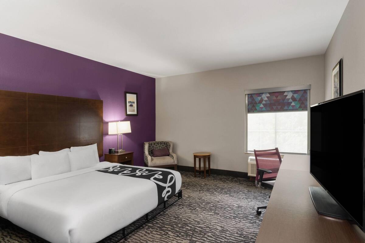 A hotel room with a bed, a desk, a chair, a television, and a window.