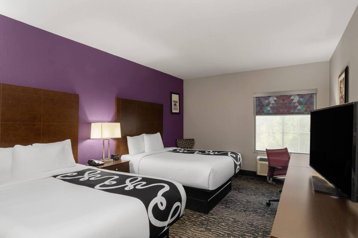 A hotel room with two beds, a desk, a television, and a window with a view.