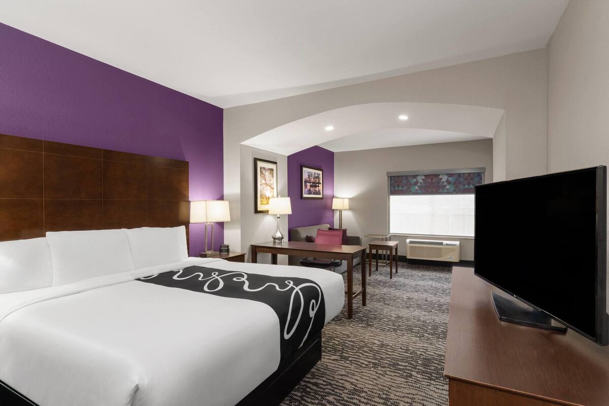 A hotel room with a large bed, a desk, a television, and a window with a view.